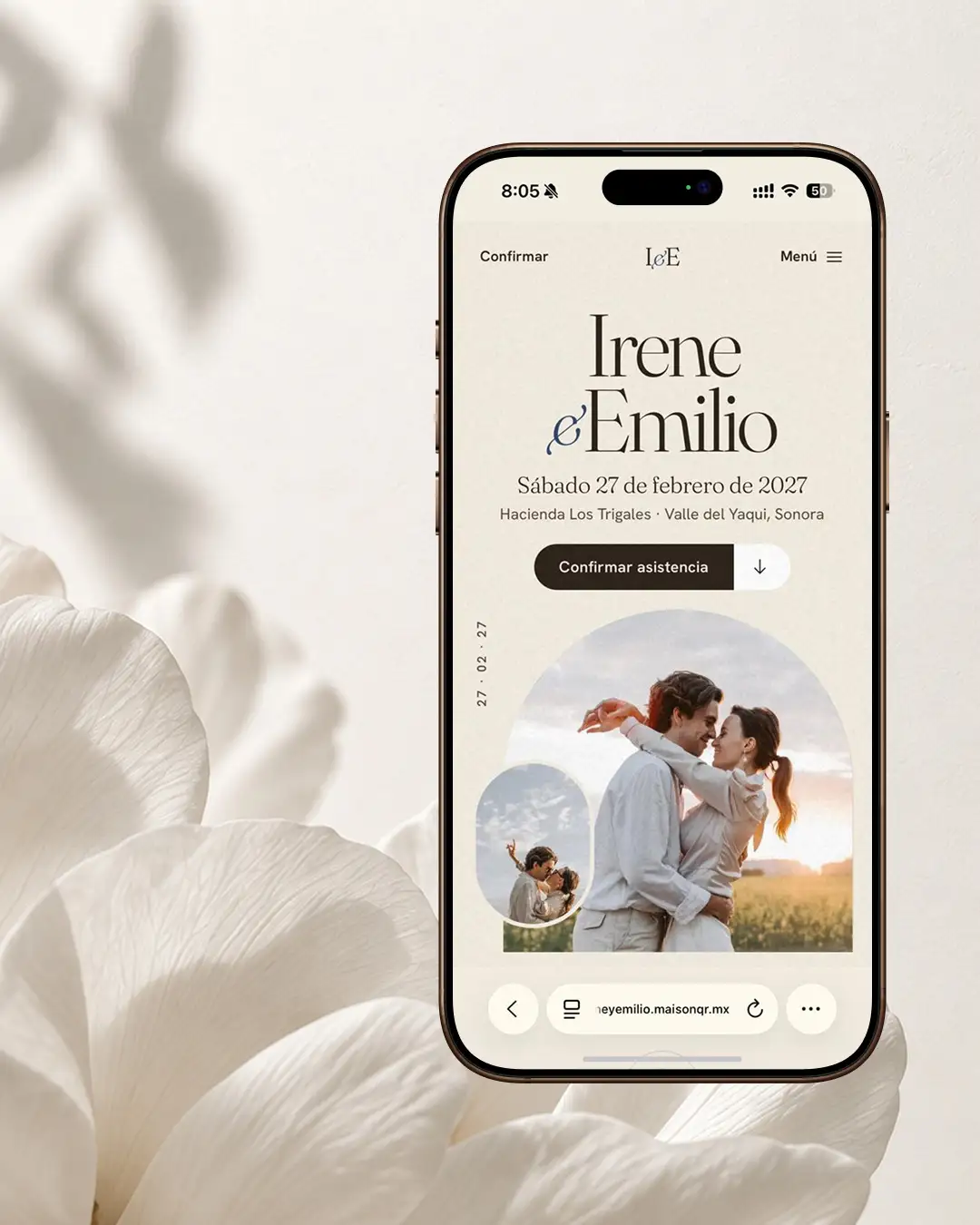 La invitación de Víspera abierta en un teléfono, de pie entre pétalos blancos y la sombra de unas hojas.